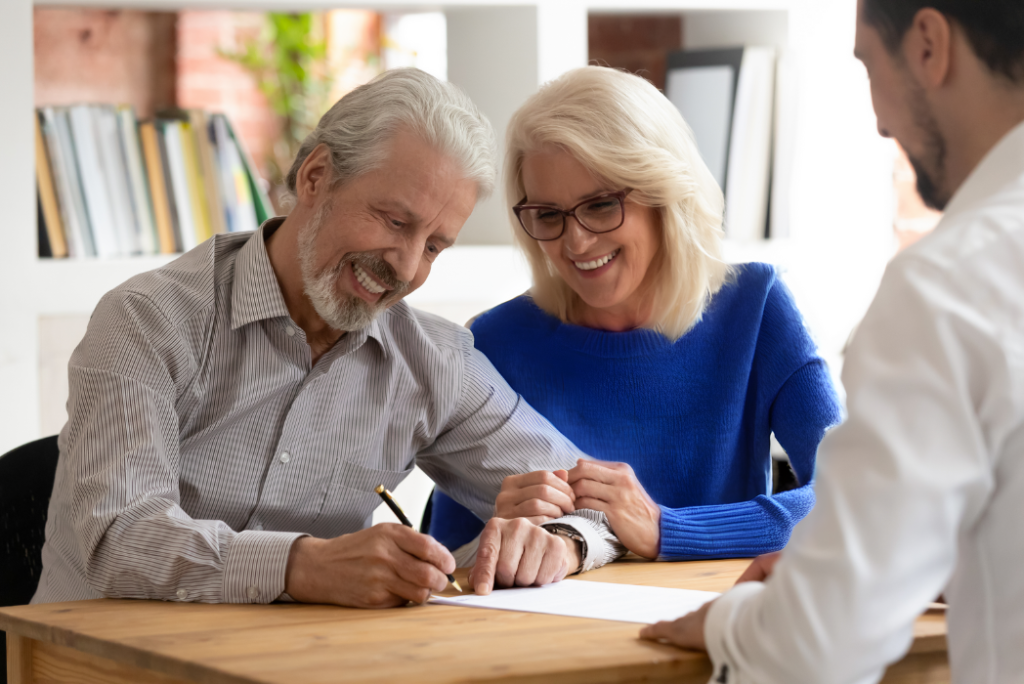 Elderly couple signing documents with an estate planning attorney, all smiling and engaged.