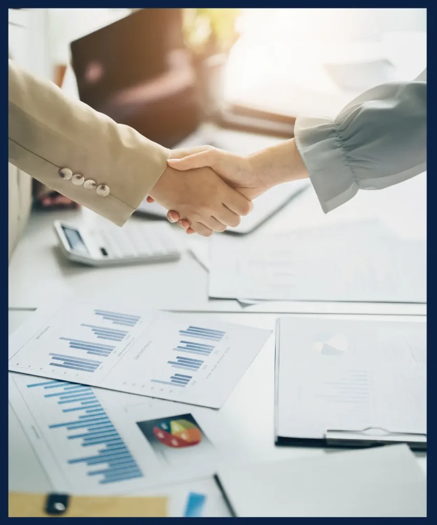 Two professionals shaking hands over financial documents, symbolizing successful business negotiations facilitated by Costaras Law.